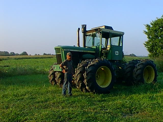 Farmer standing beside a John Deere tractor in a green field